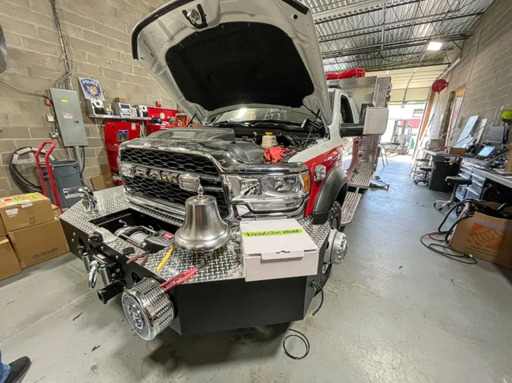 Exterior view of small fire truck showing cab, body compartments, and wheel/tire area.